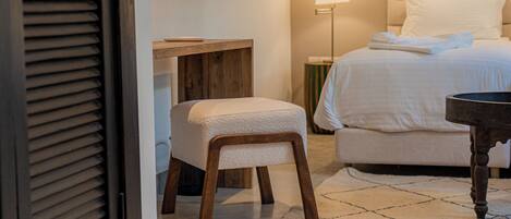 A hotel room with a bed, a bedside table, a chair, a lamp, and a door with blinds.