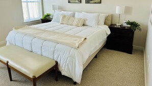 A bedroom with a large bed, a bedside table with a lamp, a bench, and two framed pictures on the wall. - Charming Modern Home Near All Magic Valley Attractions (Hollister)