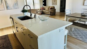 A modern kitchen with a central island, a dining area, and a living space with a sofa and curtains. - Charming Modern Home Near All Magic Valley Attractions (Hollister)