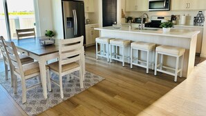 A modern kitchen with a central island, bar stools, a dining table with chairs, and a refrigerator. - Charming Modern Home Near All Magic Valley Attractions (Hollister)