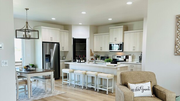 A modern kitchen with a central island, stainless steel appliances, and a dining area with a white table and bar stools. - Charming Modern Home Near All Magic Valley Attractions (Hollister)
