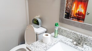 Un baño con inodoro, un rollo de papel higiénico, una botella verde y un espejo que refleja una chimenea.