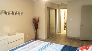 Un dormitorio con cama, cómoda, un florero con plantas secas y un pasillo que conduce a otra habitación.