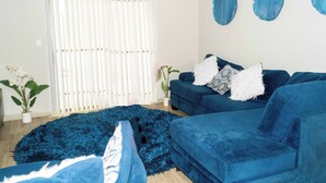 Una sala de estar con un sofá azul, un tapete azul mullido y una puerta blanca con persianas verticales.