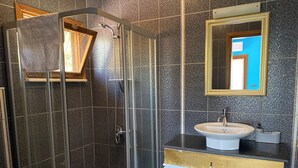 Un baño moderno con ducha de vidrio, lavamanos blanco y espejo con marco dorado.