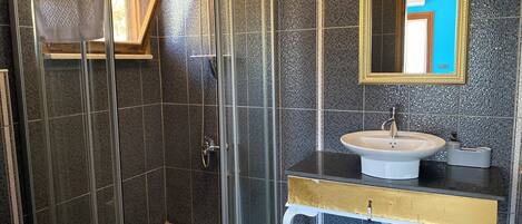 A modern bathroom with a glass-enclosed shower, a white sink, and a mirror with a gold frame.