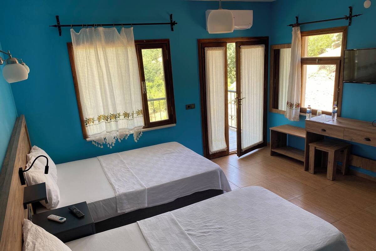 A room with two beds, a desk, a chair, a TV, and a window with curtains.
