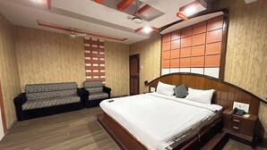 Une chambre d’hôtel avec un grand lit, une tête de lit en bois, une petite table de chevet, une commode, un plancher en bois, un ventilateur de plafond et une fenêtre avec des stores.