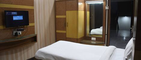 A hotel room with a bed, a wardrobe, a mirror, and a television on a shelf.