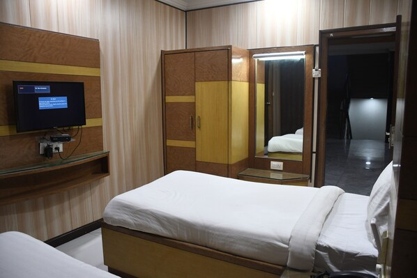 Quarto de hotel com uma cama, guarda-roupa, espelho e televisão sobre uma estante.