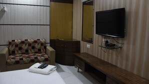 Une chambre d’hôtel comprenant un lit, un canapé, un téléviseur fixé au mur, un miroir et une armoire en bois.