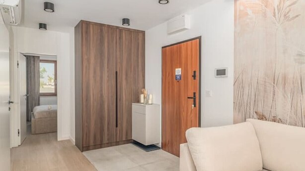 Habitació d'hotel moderna amb un sofà beix, un armari de fusta i una finestra gran.