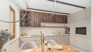 Una cuina moderna amb armaris blancs, una taula de dinar de fusta preparada per a quatre persones i un ram de flors.