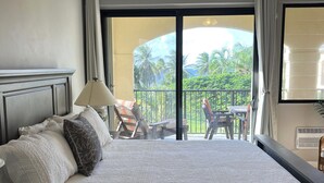 A hotel room with a large bed, a ceiling fan, and a balcony with outdoor furniture.