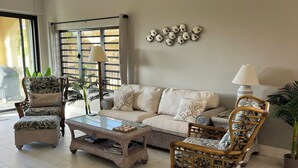 A spacious living room with a sofa, two armchairs, a coffee table, and a large window with blinds.