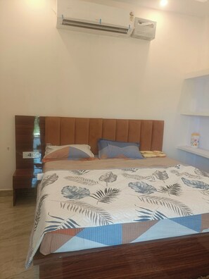 A bedroom with a bed, a nightstand, an air conditioning unit, and a wall-mounted shelf. - Madhur Kunj Guest House Pick and Drop (Faizabad)
