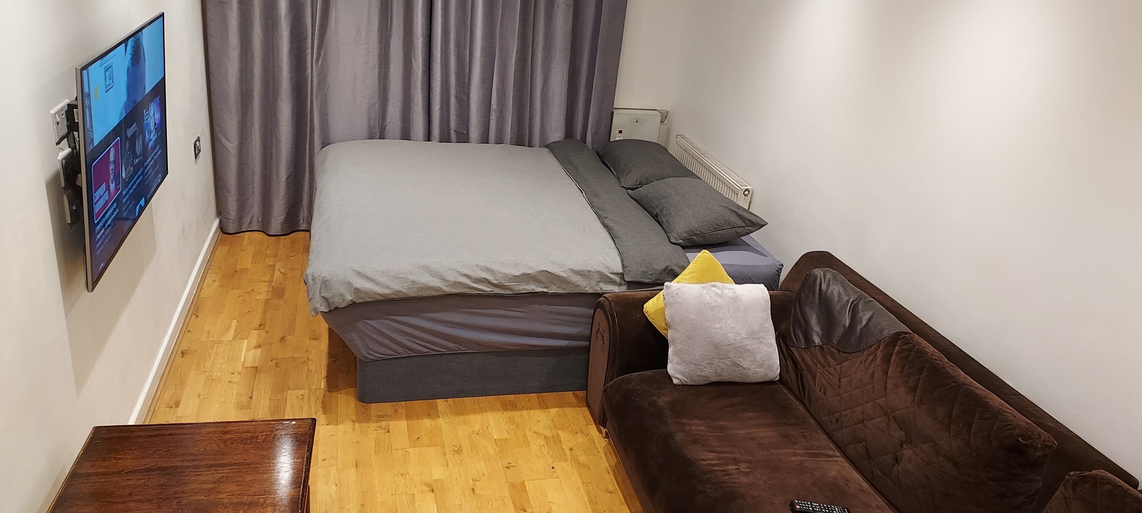 Ein Schlafzimmer mit einem Bett, einer Couch, einem an der Wand montierten Fernseher und einer Heizung.