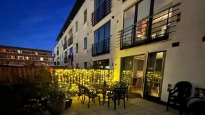 Ein Gebäude mit einer Terrassenfläche, Sitzgelegenheiten im Freien und einem gut beleuchteten Eingang.