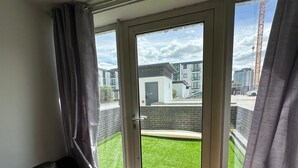 Ein Zimmer mit einer Schiebetür, die auf einen Balkon führt. Der Balkon bietet eine Rasenfläche und Blick auf Gebäude sowie einen Baukran.
