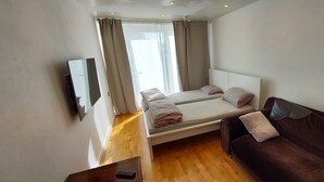 Ein Schlafzimmer mit einem Bett, einem braunen Sofa, einem Fernseher und einem Fenster mit Vorhängen.