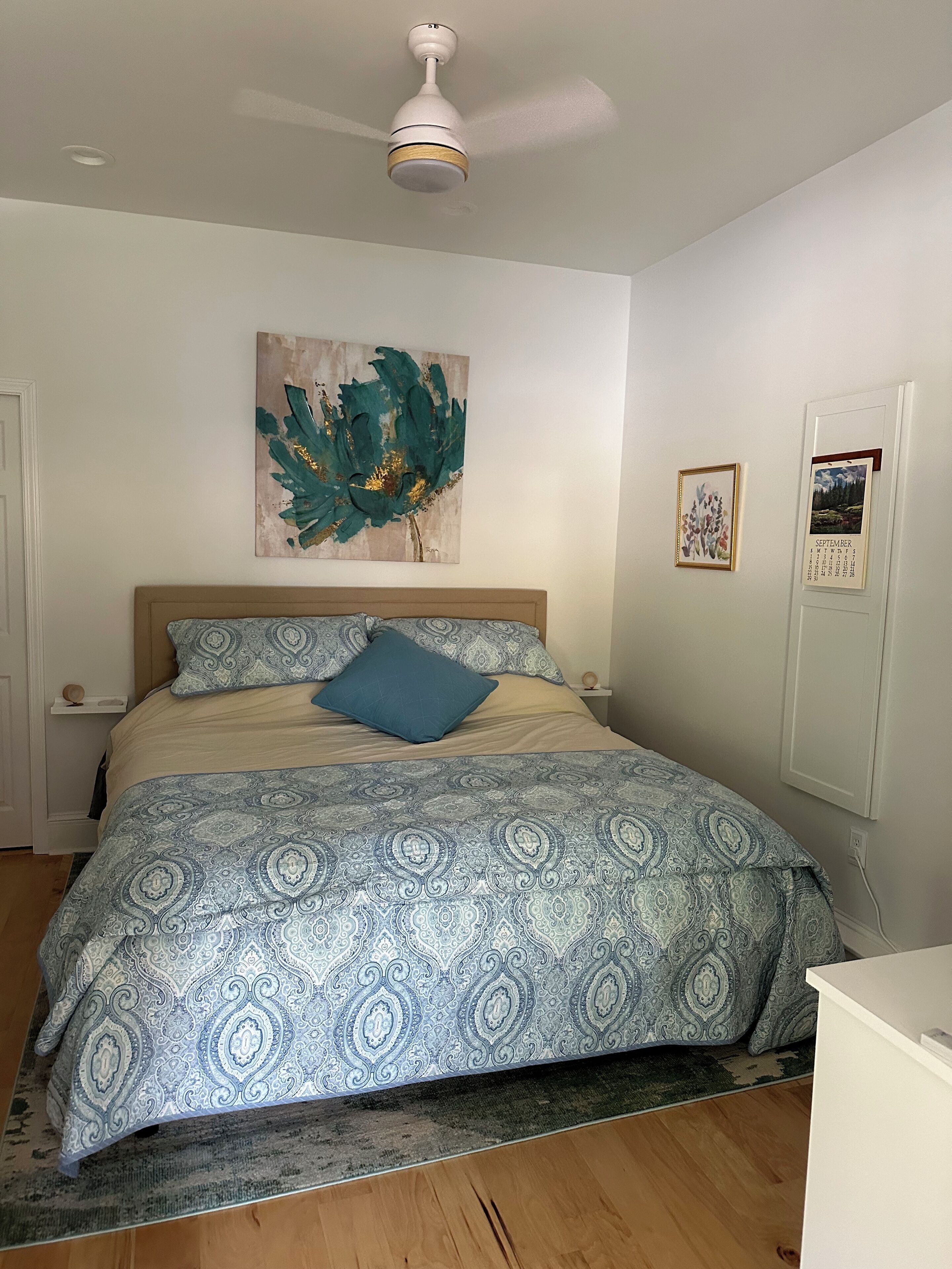 Un dormitorio con una cama, ventilador de techo, un reloj de pared y un calendario.