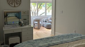 Une chambre à coucher avec un lit, un bureau avec un ordinateur, une chaise, un arbre à chat et une vue sur l’extérieur.