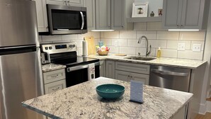 Une cuisine moderne avec des meubles gris, des appareils en acier inoxydable, un plan de travail en granit et un îlot central doté de deux chaises.
