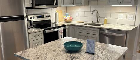 A modern kitchen with grey cabinets, stainless steel appliances, a granite countertop, and a central island with two chairs.
