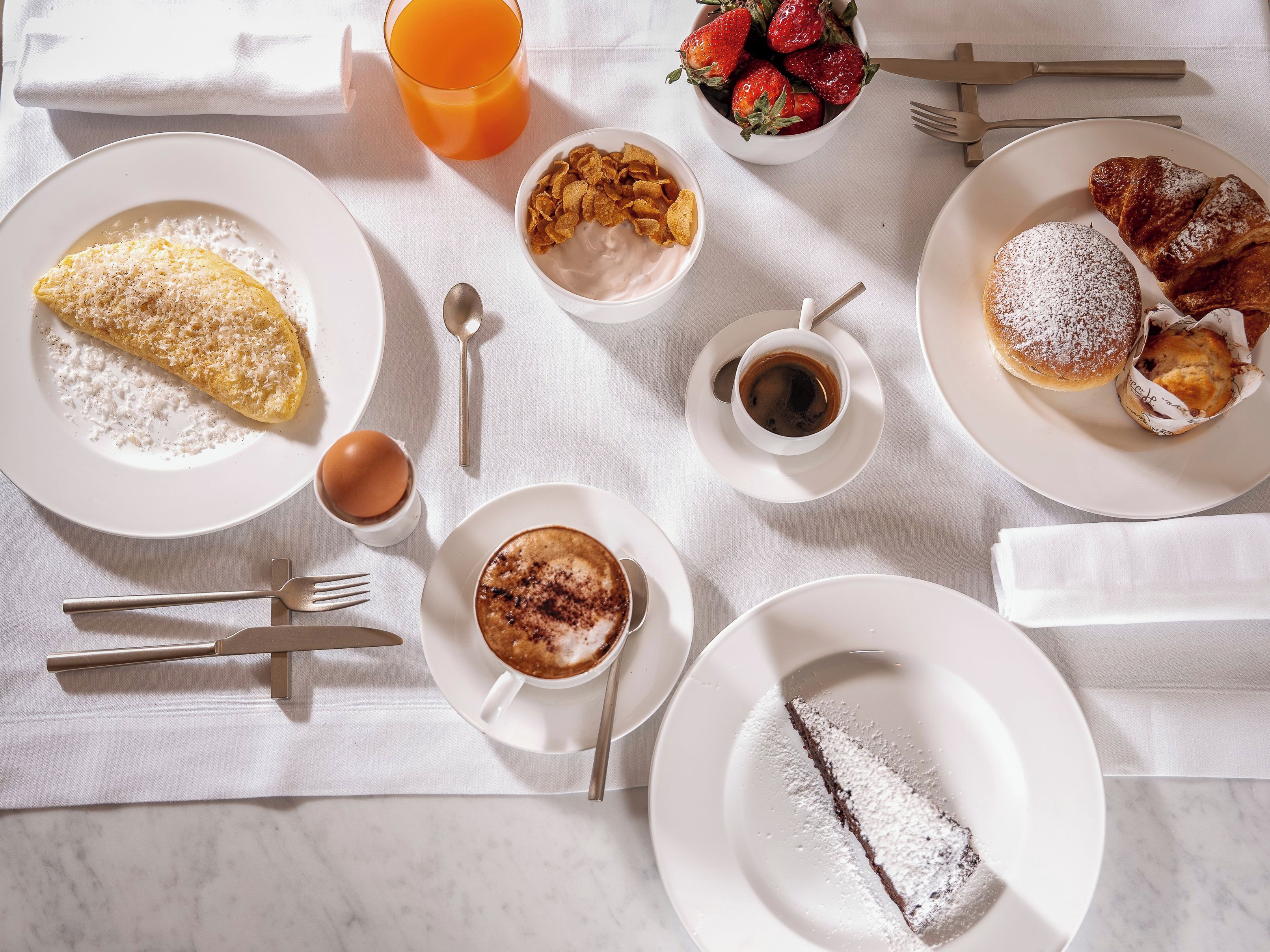 A breakfast setting with various dishes including an omelette, strawberries, cereal, coffee, and pastries.