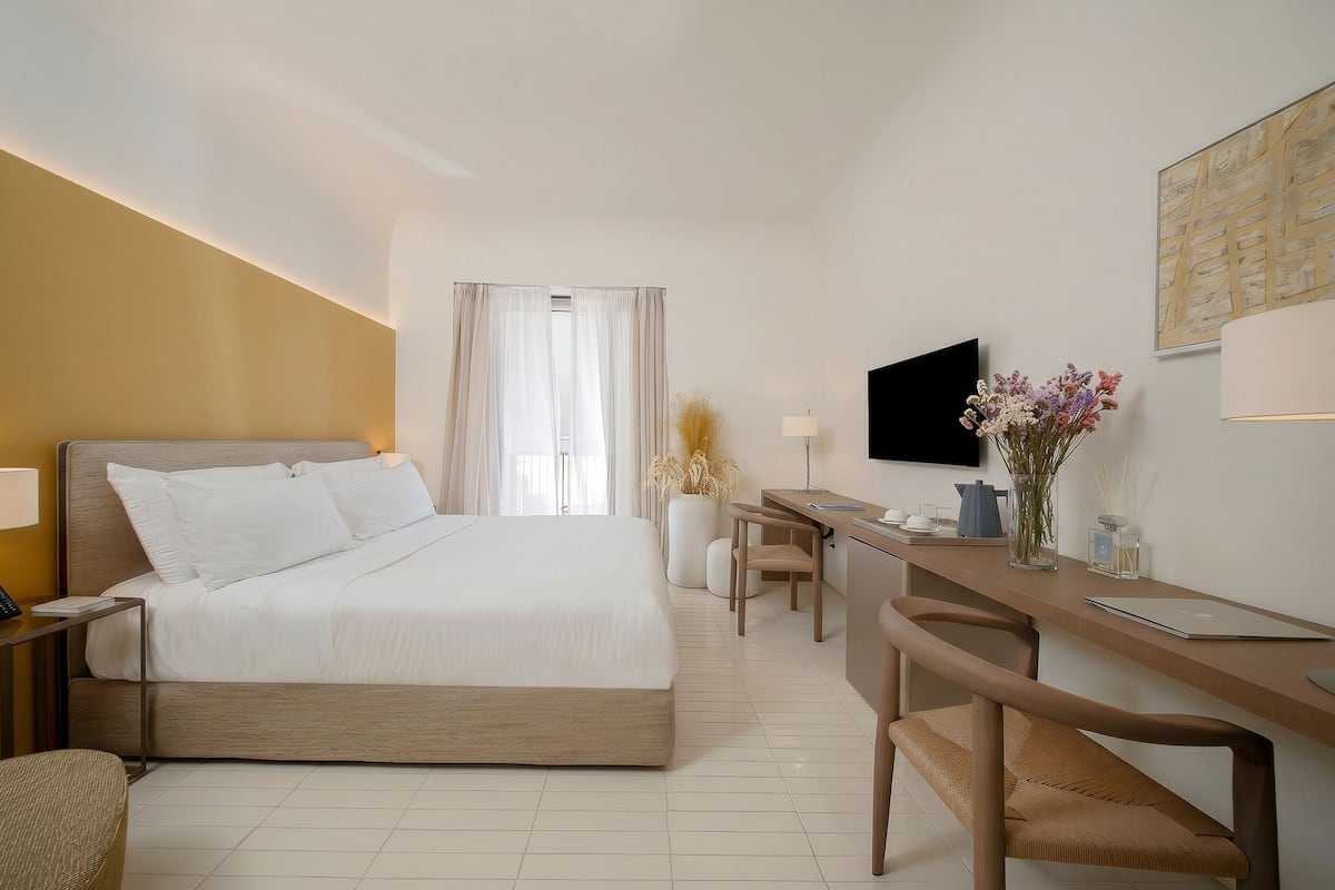 A hotel room with a bed, desk, chair, TV, and a window with curtains.