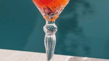 A clear glass cocktail with a lemon slice garnish, placed on a marble surface near a pool.
