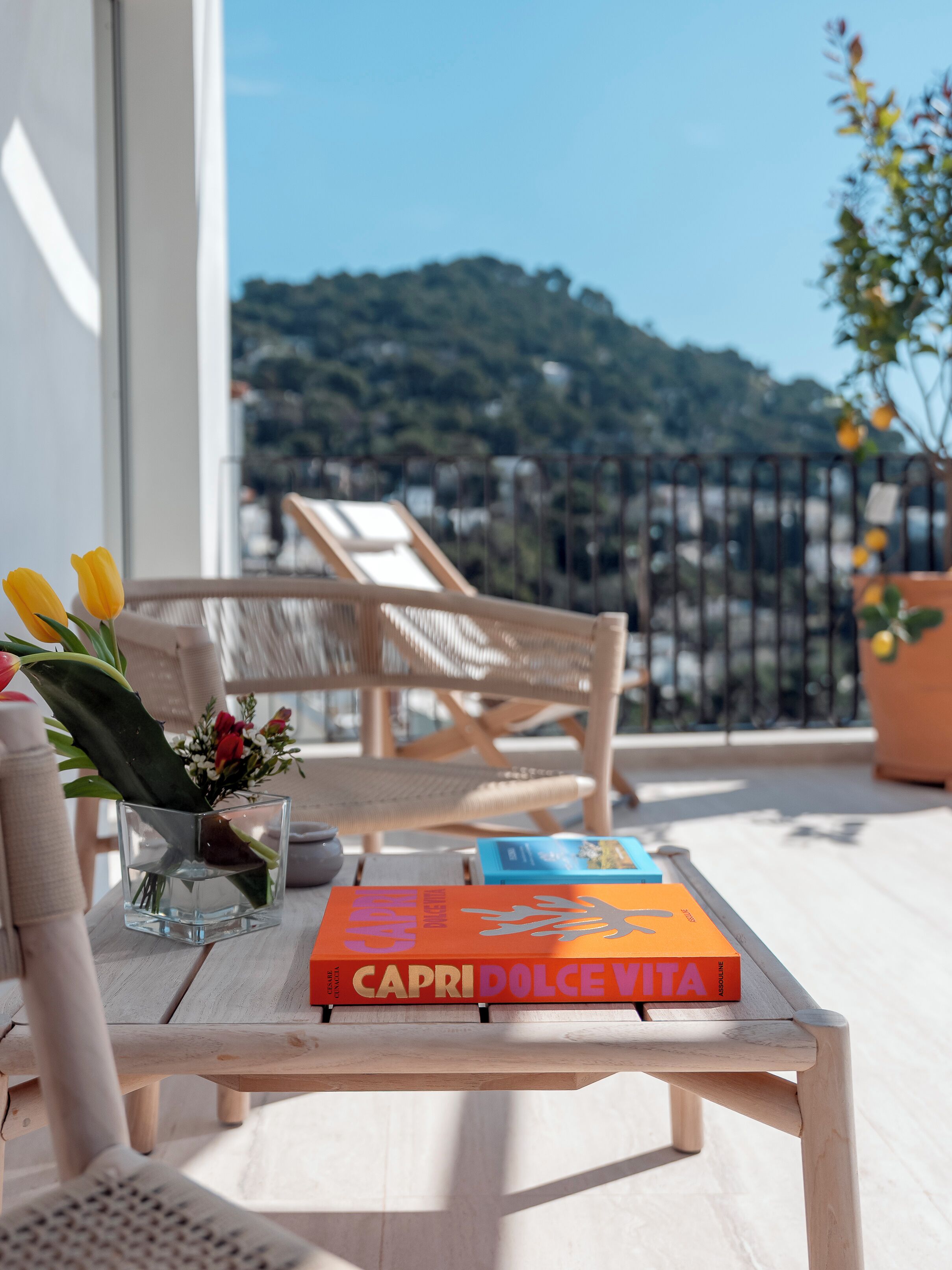 Una mesa de madera con un libro titulado "CAPRI DOLCE VITA" y un jarrón con flores.