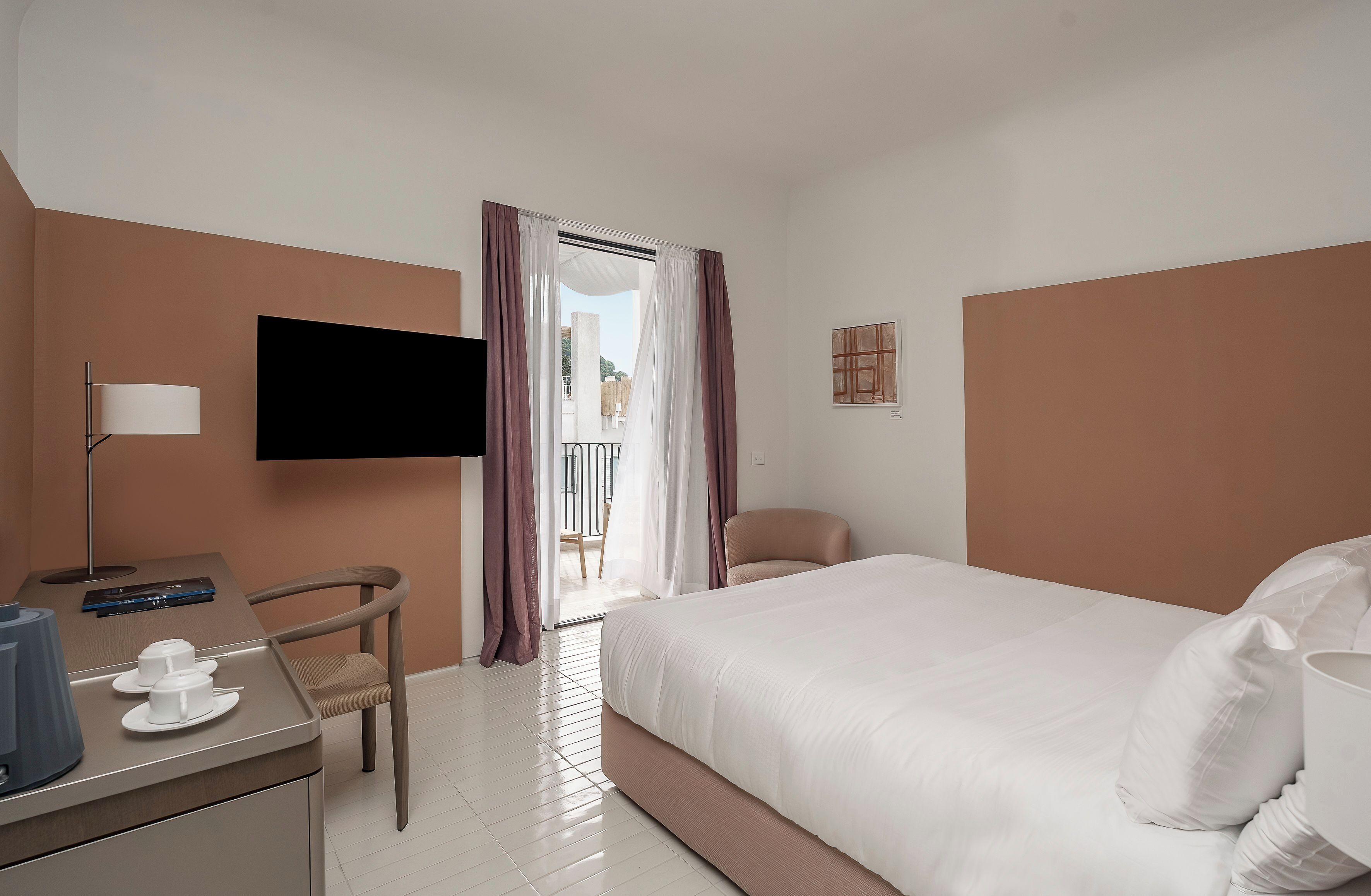 Una habitación de hotel con cama, escritorio con silla, televisor y vistas al exterior.