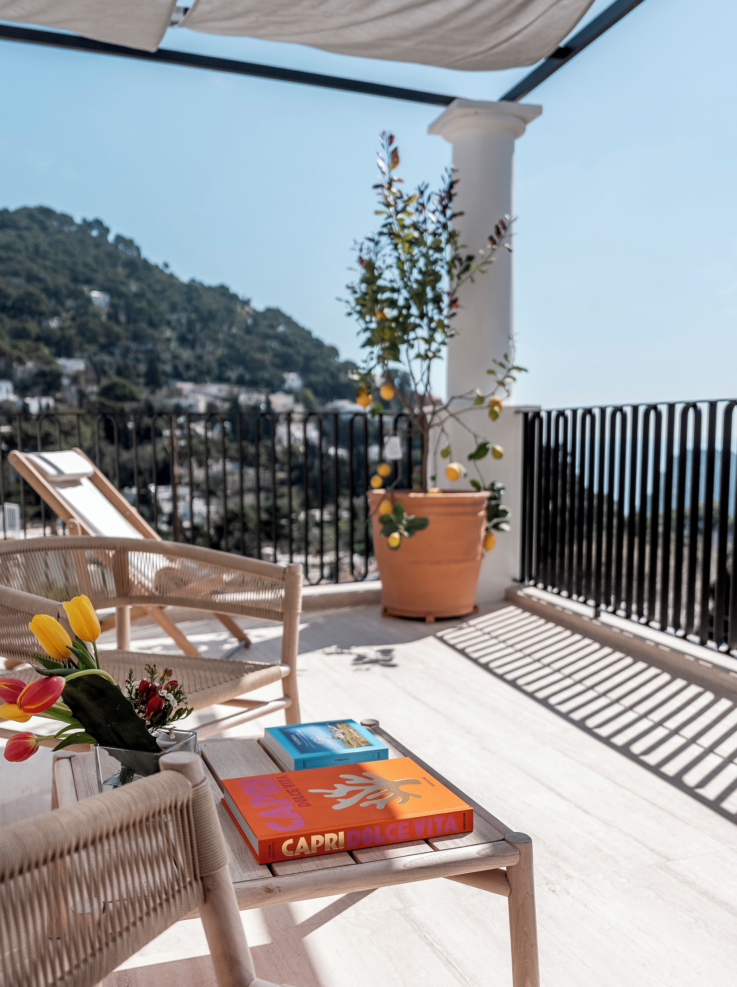 Un balcon avec un fauteuil en osier, une plante en pot et un livre intitulé « Capri Dolce Vita ».