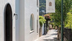 Eine enge Straße mit einem weißen Gebäude, einem hängenden Schild für Villa Certosa Capri und einem Laternenpfahl.