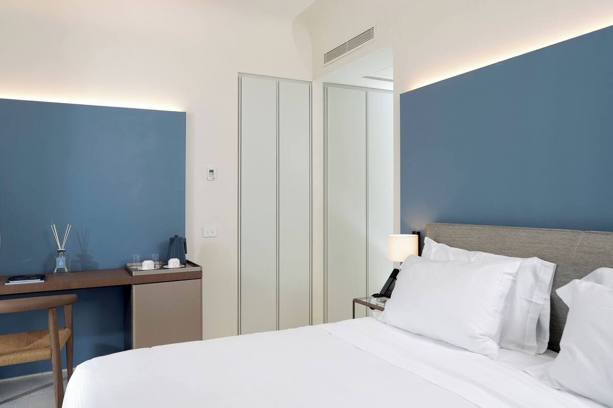 A hotel room with a bed, a desk, a chair, a nightstand, and a wardrobe.