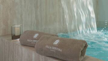 Un baño con pared de mármol, un perchero con toallas y un recipiente de vidrio.