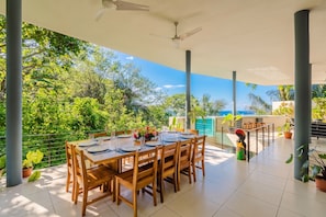 Un área de comedor al aire libre con una mesa preparada para cuatro personas, rodeada de plantas en macetas y vista al mar.