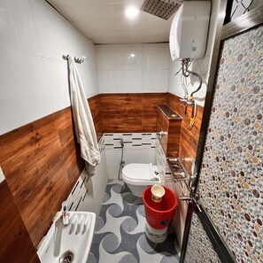 A compact bathroom with a wooden accent wall, a white toilet, a sink, and a shower area.
