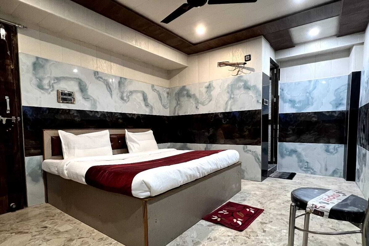 A modern bedroom with a large bed, marble flooring, a ceiling fan, and a small stool.
