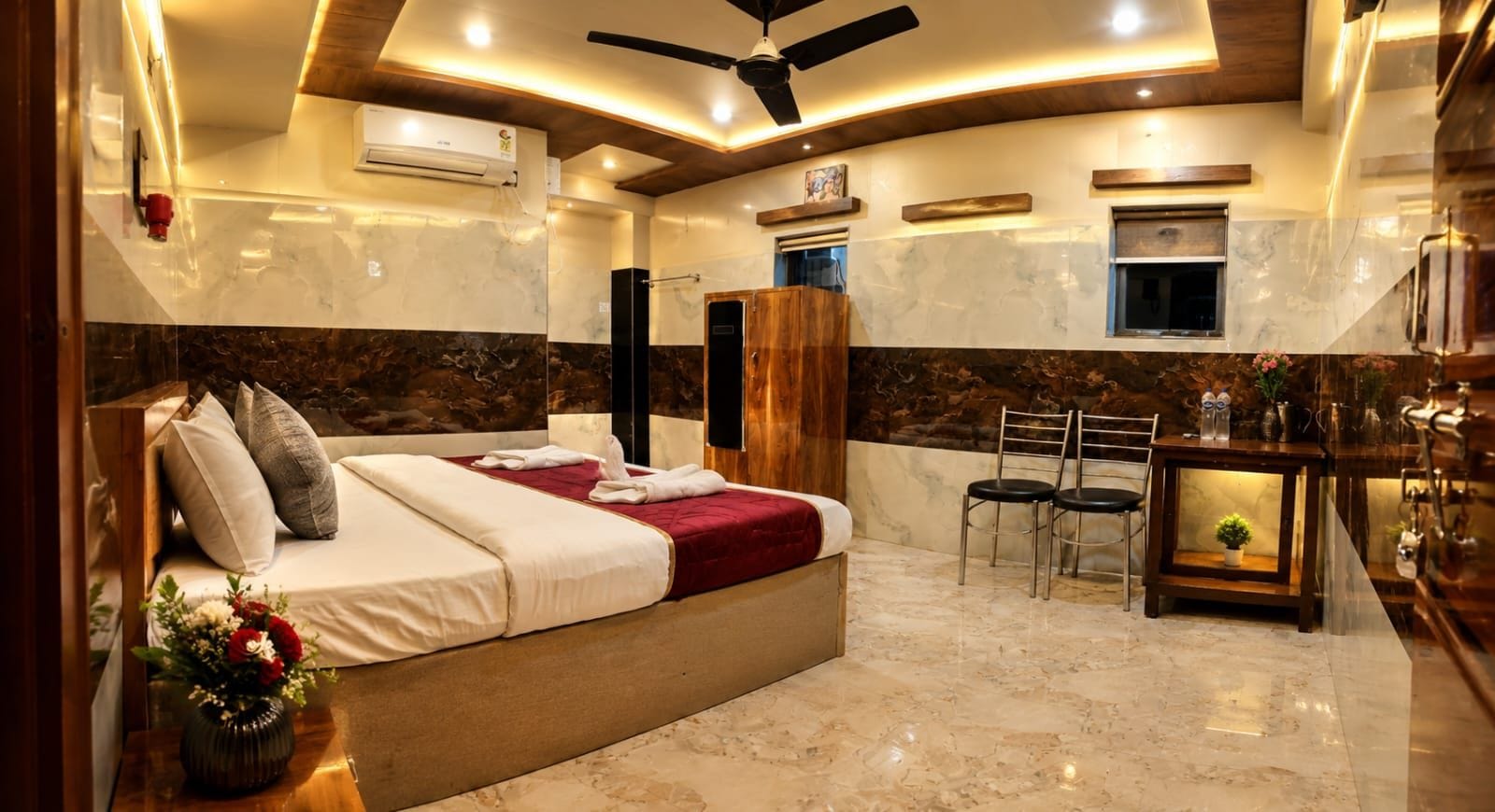 A hotel room with a bed, a desk, chairs, a ceiling fan, and a wall-mounted air conditioner.