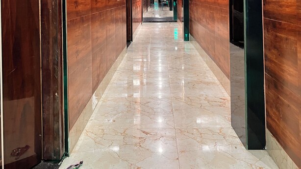 Corredor com paredes de madeira e chão de mármore, que leva a um elevador.