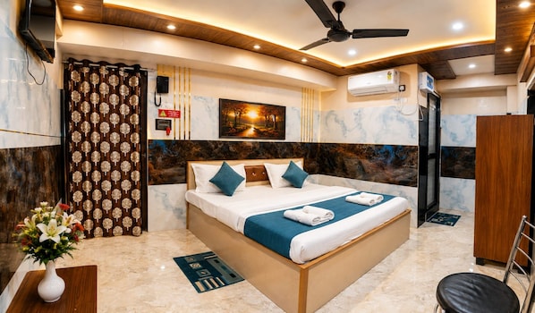 A hotel room with a bed, a ceiling fan, an air conditioning unit, and a painting on the wall.