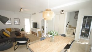 Una sala moderna con una mesa de comedor de madera, sillas negras, un sofá gris con cojines amarillos, un televisor y un espejo grande.