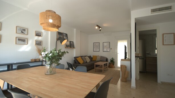 Un salón moderno con una mesa de comedor de madera, un sofá y una lámpara colgante.