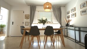 Un comedor con una mesa de madera, cuatro sillas, una lámpara colgante, una ventana con cortinas y una pared decorada con cuadros.
