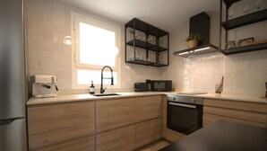 Una cocina moderna con armarios de madera, horno empotrado, microondas y ventana que deja entrar luz natural.