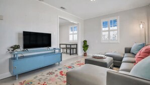 A modern living room with a flat-screen TV, a blue dresser, a gray sofa, and a floral rug. - 4BR/3BA Retreat - Perfect for Families & Groups (Tybee Island)