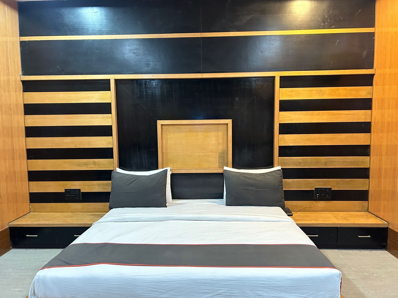 A modern bedroom with a large bed, wooden paneling, and built-in storage drawers.
