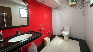 A bathroom with a red wall, a black sink, a mirror, a toilet, and a shower. - SwagStay Hotel Rahul Palace Nagpur (Nagpur)